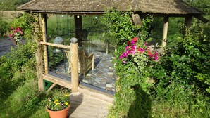A gazebo with a tiled floor and a wooden railing, surrounded by lush greenery and flowering plants. - Black Burn Lodge (Newcastleton)