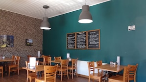 A restaurant interior with wooden tables and chairs, a stone wall, and a menu board on the wall. - Black Burn Lodge (Newcastleton)
