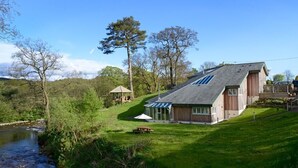 A house with a sloped roof, a small garden, and a picnic table. - Black Burn Lodge (Newcastleton)