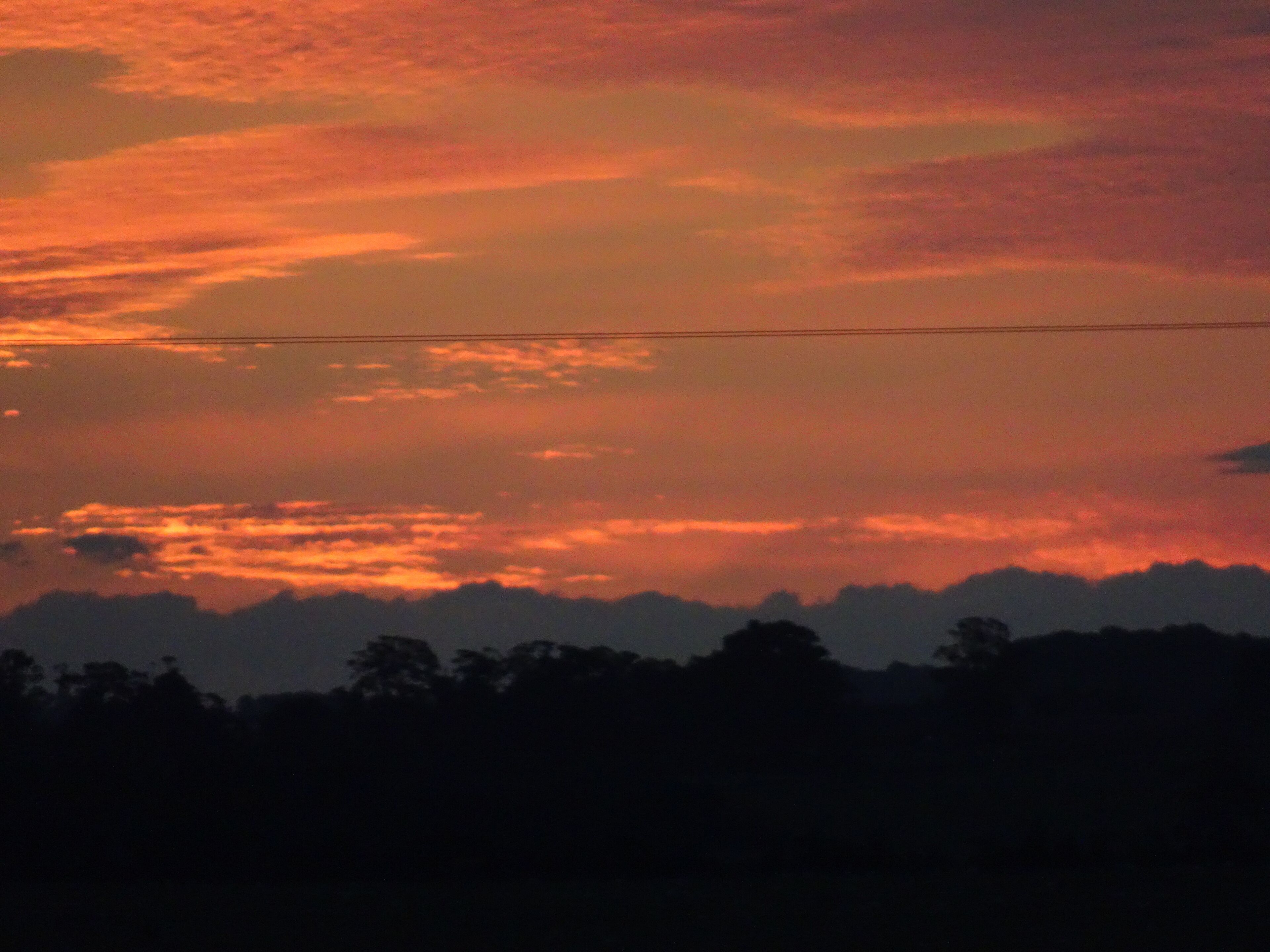 Un coucher de soleil avec une ligne électrique qui traverse le ciel.