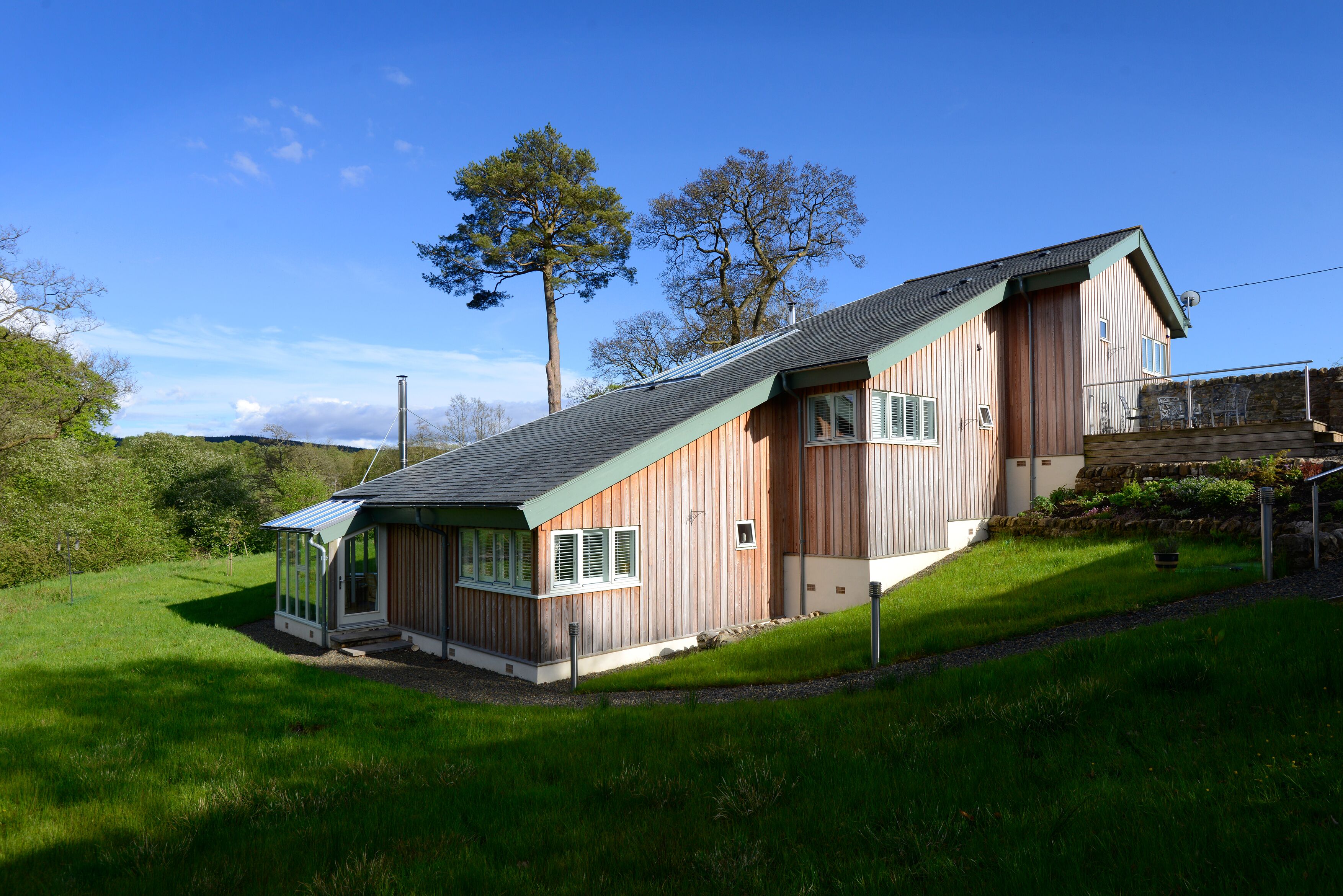 A wooden house with a sloped roof, a covered porch, and a stone wall.