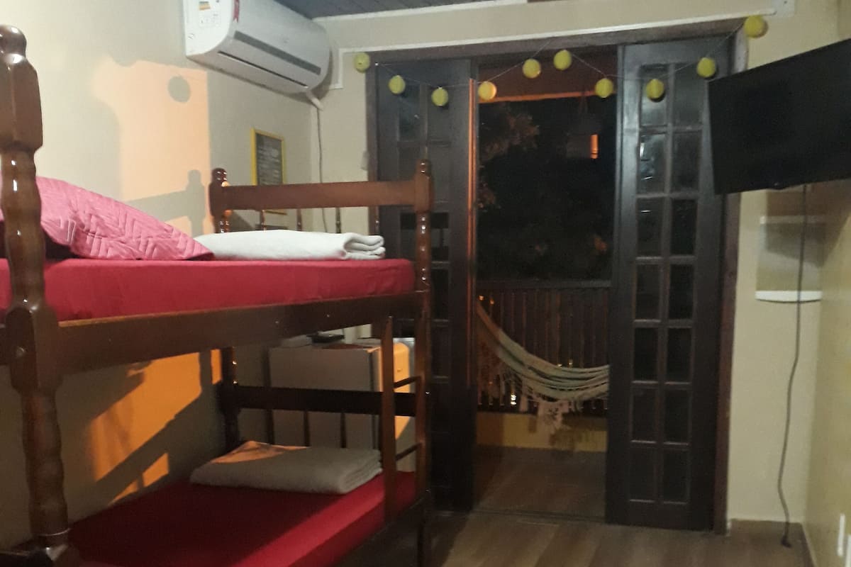 A room with a bunk bed, a small rug, and a doorway leading to a balcony with a hammock.