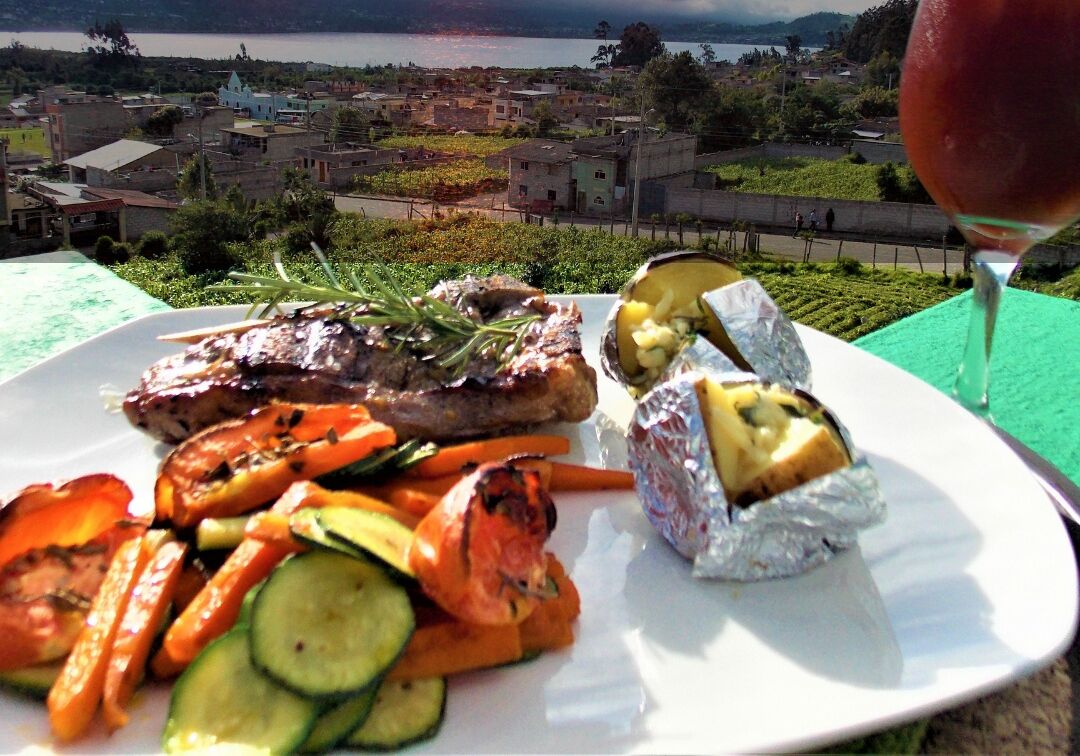 A plate of grilled meat, vegetables, and foil-wrapped food with a scenic view in the background.