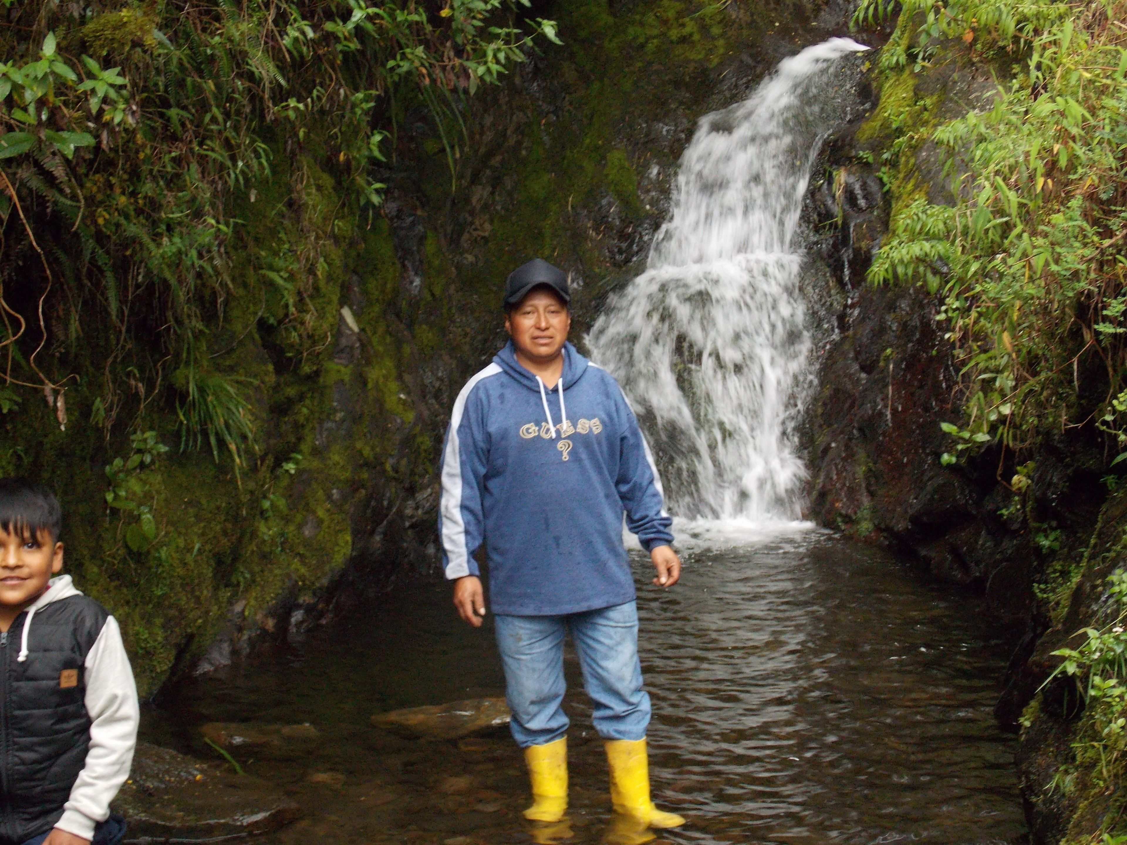 Une personne se tient dans un environnement naturel, avec une cascade en arrière-plan.