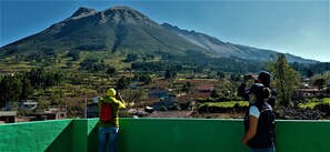 A view of a mountain from a green-roofed building with a person taking a photo. - Green House Araque Inn (San Pablo del Lago)