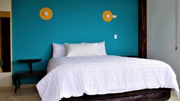 Una cama con cubrecama blanco en una habitación con paredes color turquesa y un banco de madera.