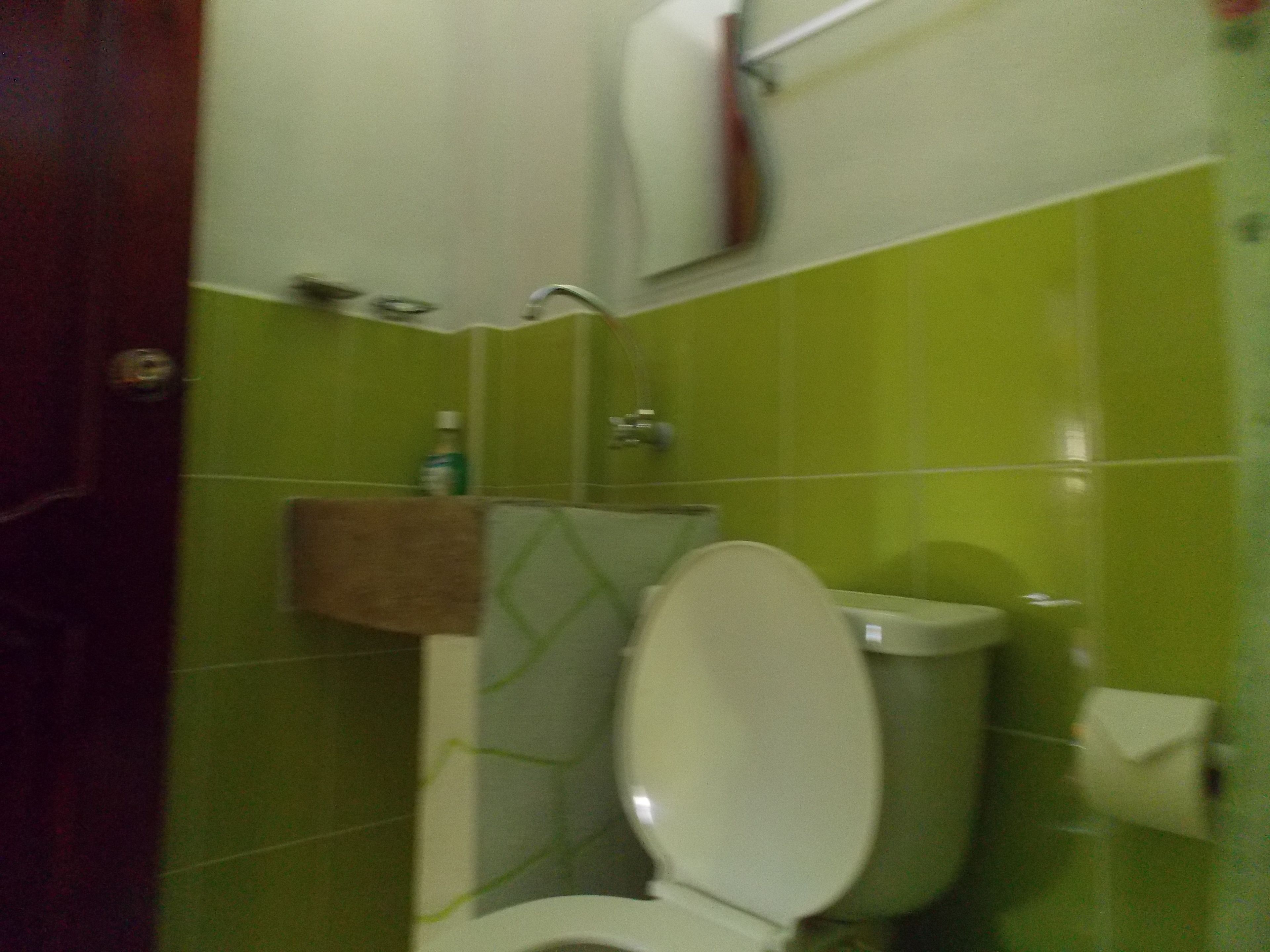 A bathroom with green tiles, a white toilet, a towel rack, and a soap dispenser.