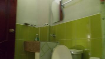 A bathroom with green tiles, a white toilet, a towel rack, and a soap dispenser.