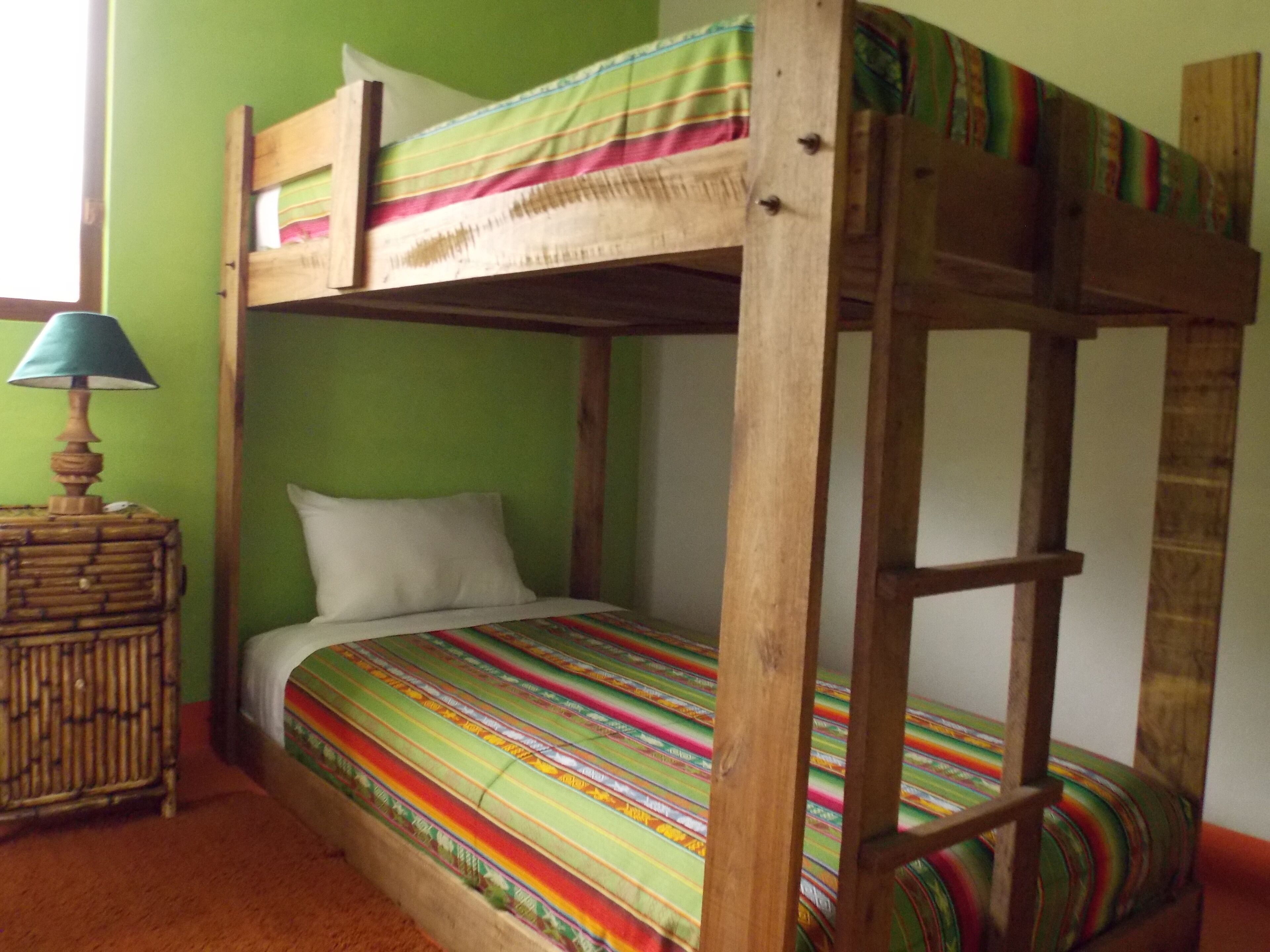 Una cama litera con una colcha a rayas de colores, un cabecero de madera y una mesita de noche con una lámpara.
