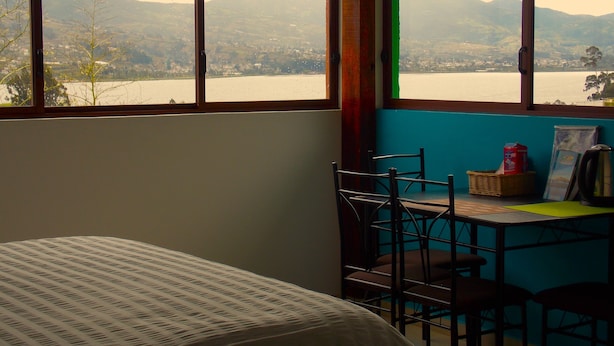 A room with a bed, a table with chairs, a window with a view of mountains and a lake, and a wall with a blue accent. - Green House Araque Inn (San Pablo del Lago)