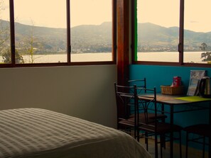 A room with a bed, a table with chairs, a window with a view of mountains and a lake, and a wall with a blue accent. - Green House Araque Inn (San Pablo del Lago)