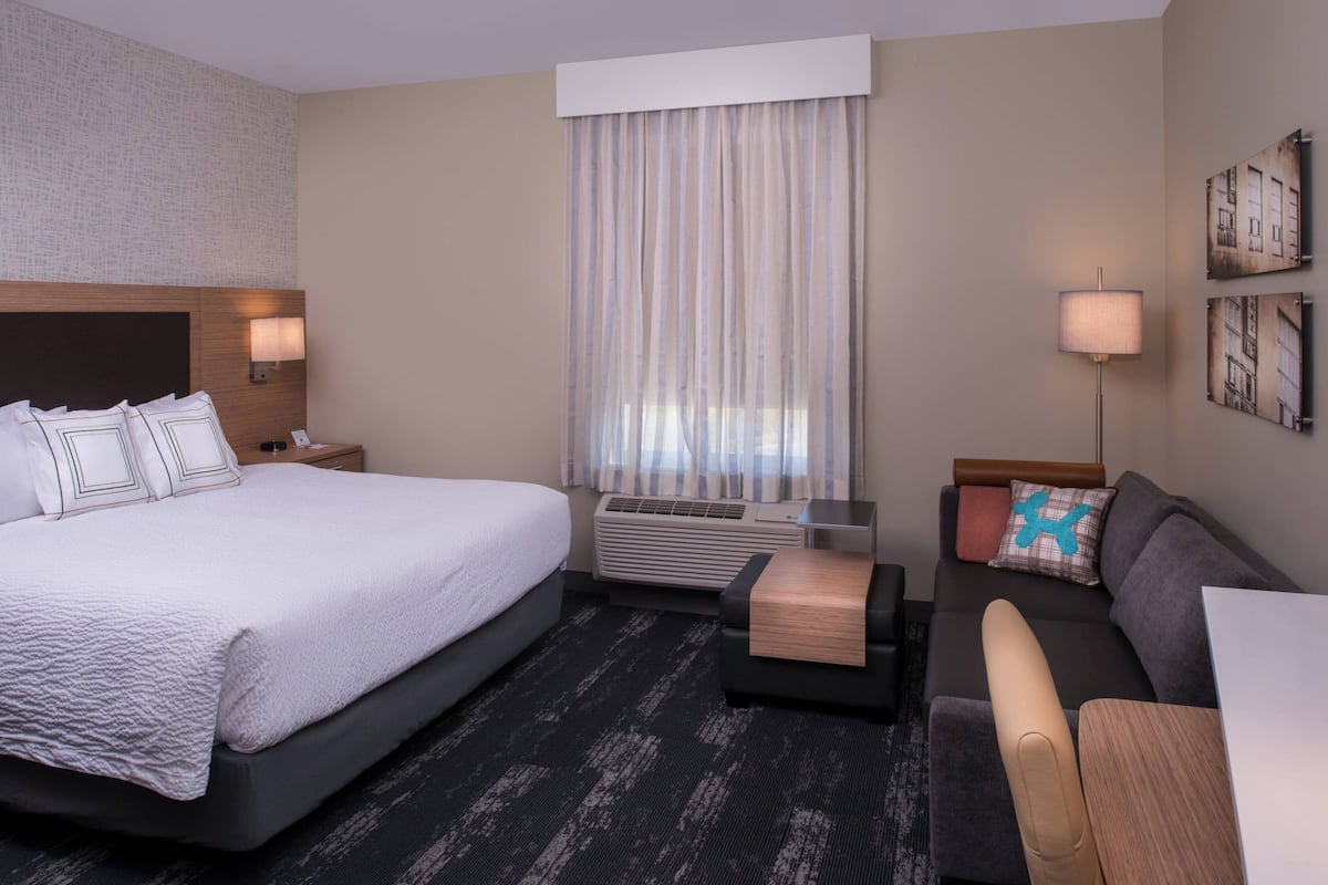 A hotel room with a large bed, a sofa, a desk, and a window with curtains.