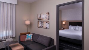 A hotel room with a sofa, a bed, a lamp, and artwork on the wall. - TownePlace Suites by Marriott Saskatoon (Saskatoon)
