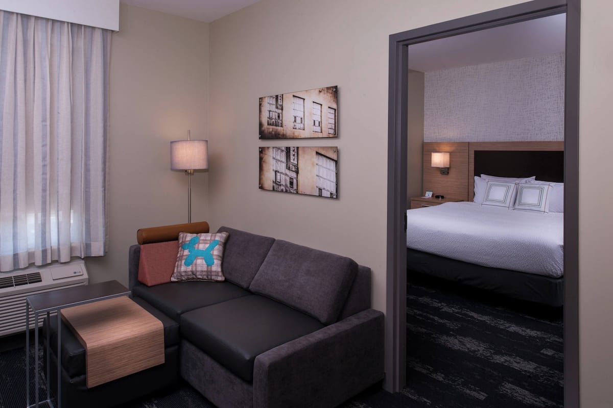A hotel room with a sofa, a bed, a lamp, and artwork on the wall.
