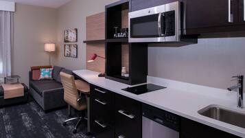 A modern kitchen with a microwave, sink, and built-in cabinets. There is a small seating area with a couch and a desk.