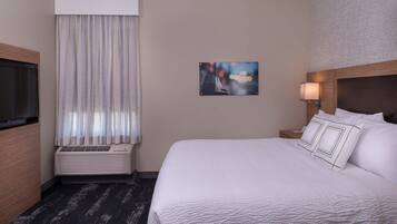 A hotel room with a bed, a TV, an air conditioner, a window with curtains, and a painting on the wall.