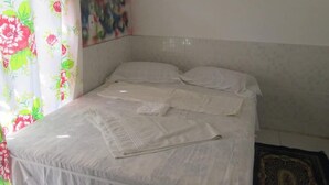 Una cama con sábanas blancas, una cortina floral y un cuadro en la pared.