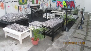 Un área de estar al aire libre con bancos y cojines a cuadros blancos y negros de cebra, rodeada por un muro decorativo con banderas y flores.