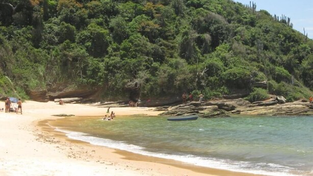 Una playa con aguas cristalinas, orilla arenosa y una colina boscosa al fondo.