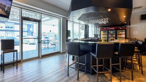 Een moderne bar met een groot raam, barstoelen en een Coca-Cola koelkast.