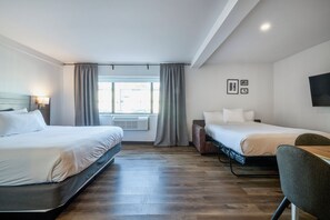 Habitación de hotel con dos camas, un escritorio, una silla y un televisor en la pared.