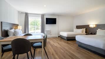 A hotel room with a bed, a desk with a chair, a TV mounted on the wall, and a window with curtains.