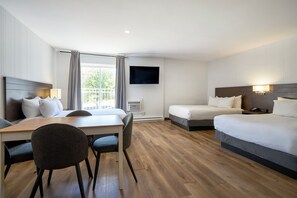 Una habitación de hotel con cama, escritorio y silla, televisor montado en la pared y ventana con cortinas.