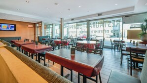 Een restaurant met meerdere tafels en zitjes, een televisiescherm en grote ramen.