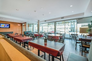A restaurant with multiple tables and booths, a television screen, and large windows. - Hôtel Newstar Montréal (Montreal)