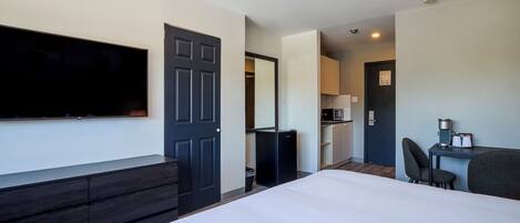 A hotel room with a bed, a TV, a desk with a chair, a kitchenette, and a bathroom.