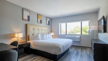 Una camera d'albergo con un letto, comodini, una scrivania, una sedia, una televisione e una finestra vista.