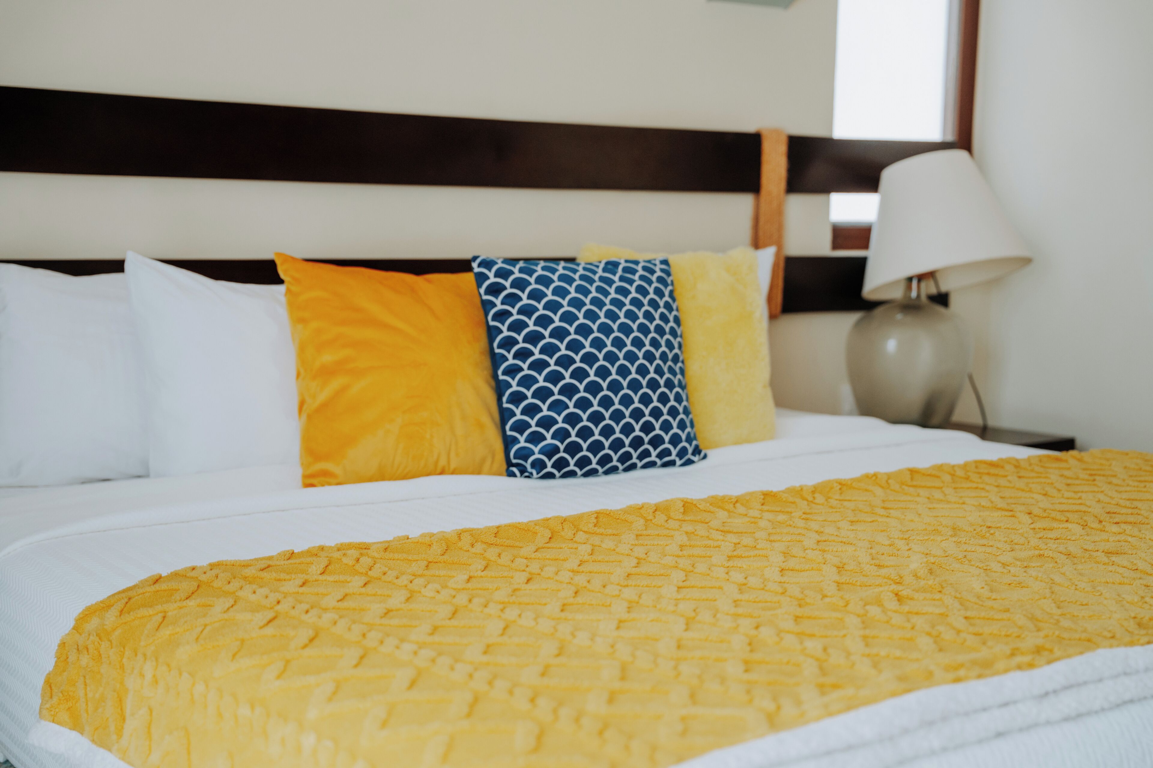 A neatly made bed with a yellow textured blanket, white pillows, and a blue patterned pillow.