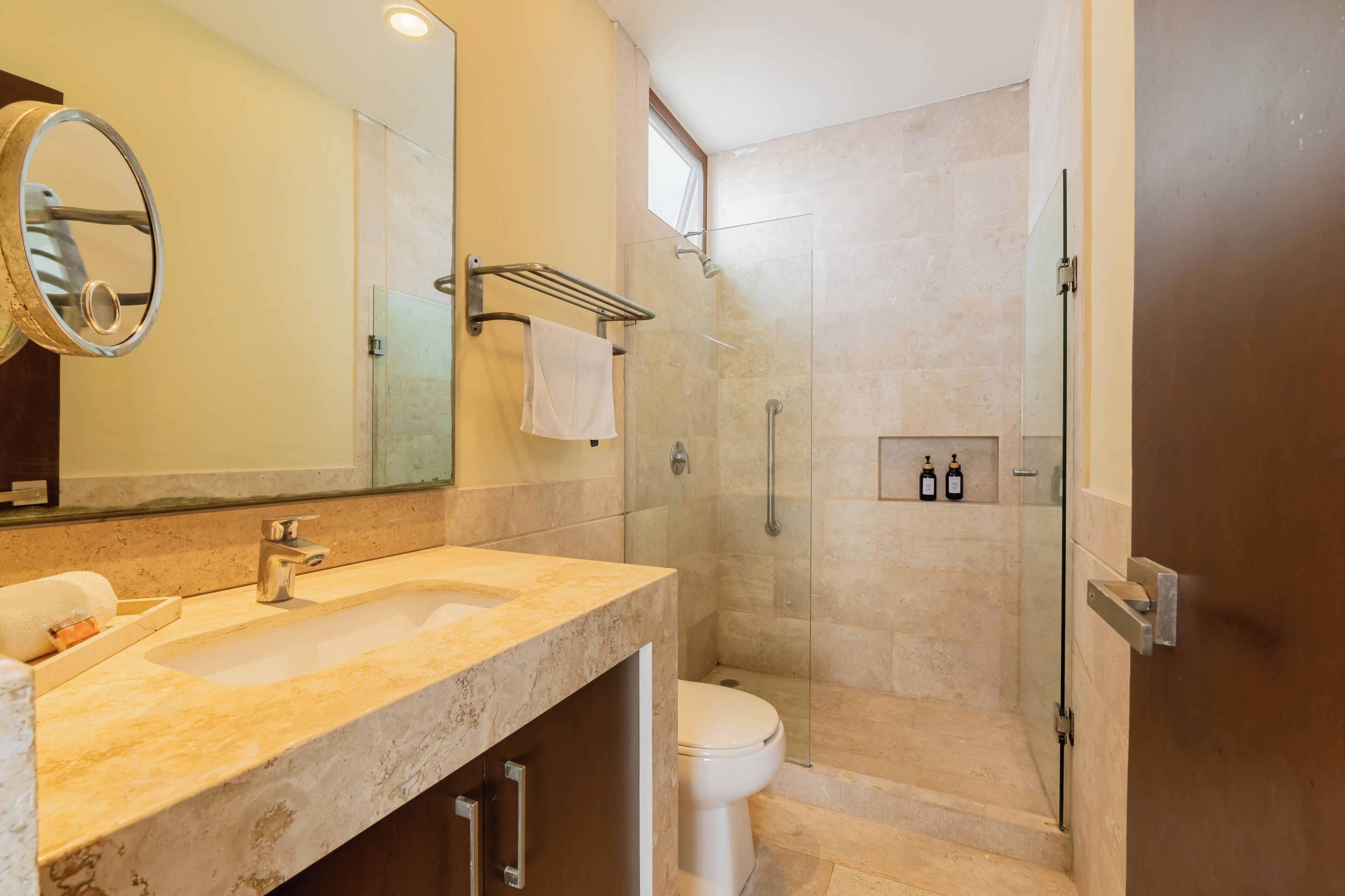 Un baño con lavamanos de mármol, inodoro, ducha con puerta de vidrio y toallero.