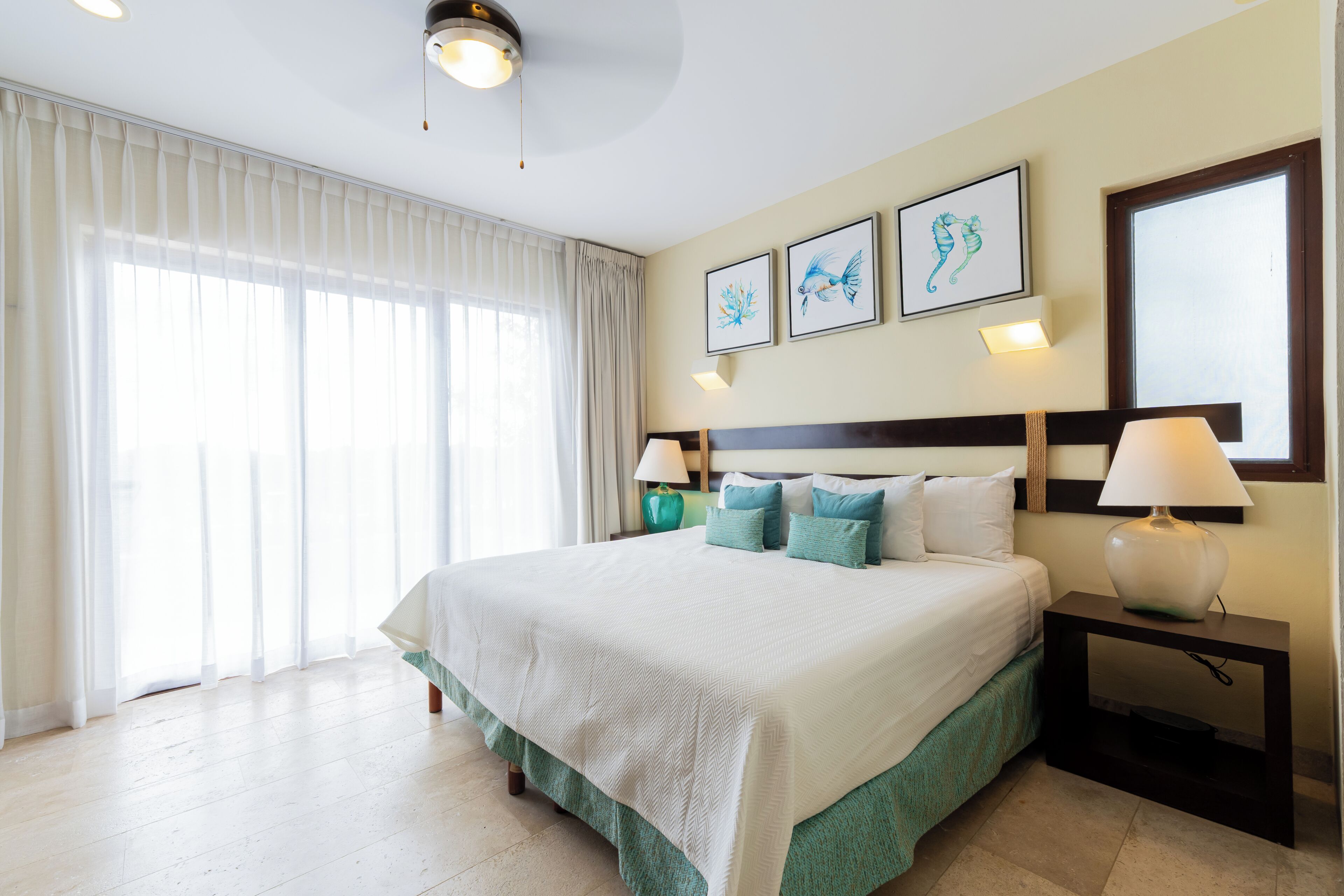 A hotel room with a large bed, two bedside lamps, a nightstand, and a window with sheer curtains.