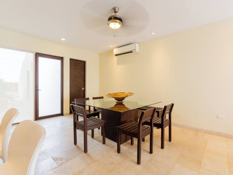 A dining area with a glass table, wooden chairs, and a ceiling fan.