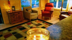 A cozy cabin interior with a wooden floor, a patterned rug, a glass candle holder with a lit candle, and two leather chairs. - Rolling Hills Lodge (Cherokee)