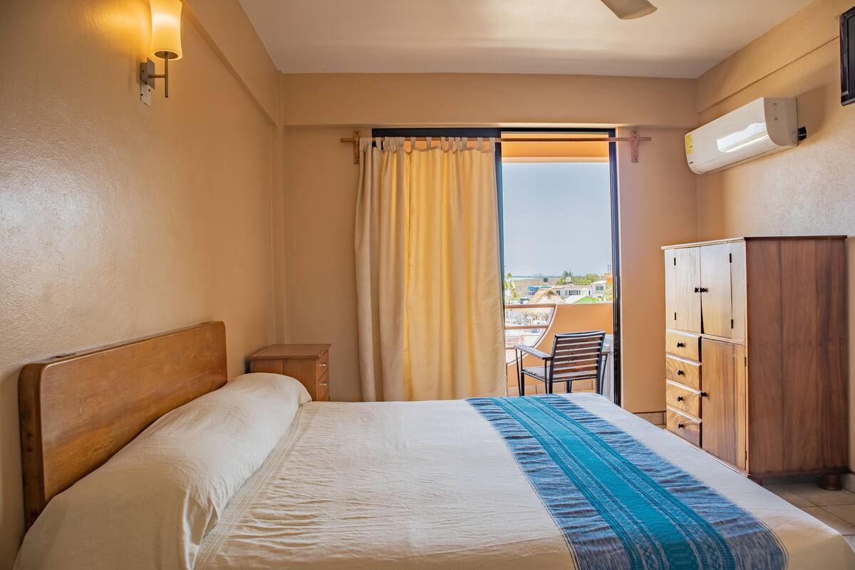 A hotel room with a bed, a wooden wardrobe, a desk, and a chair.