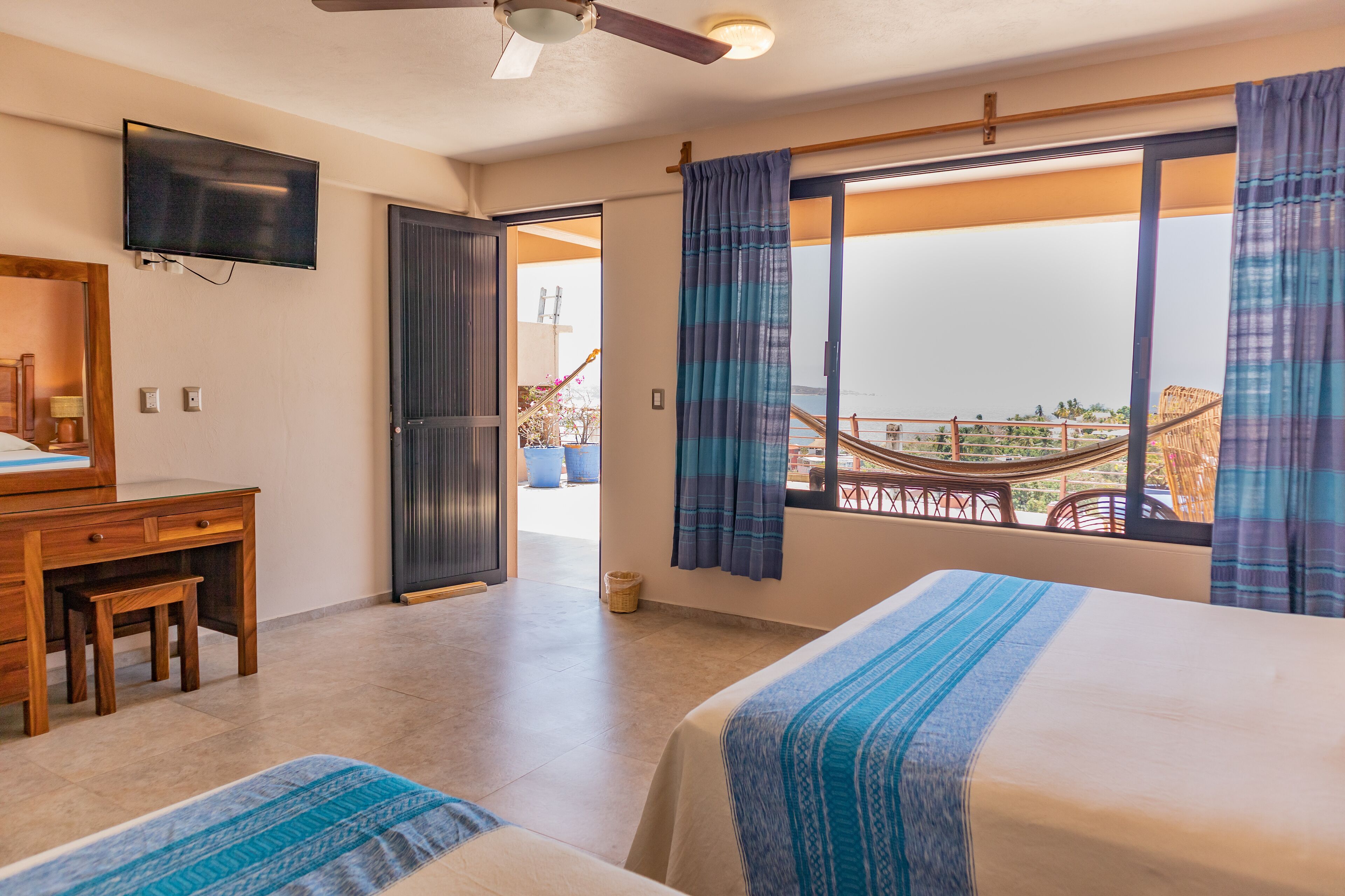 Habitación de hotel con cama, escritorio, televisión y balcón con vista a un puente.