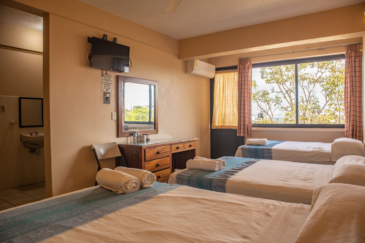 A hotel room with two beds, a desk with a mirror, a sink, and a window with curtains.