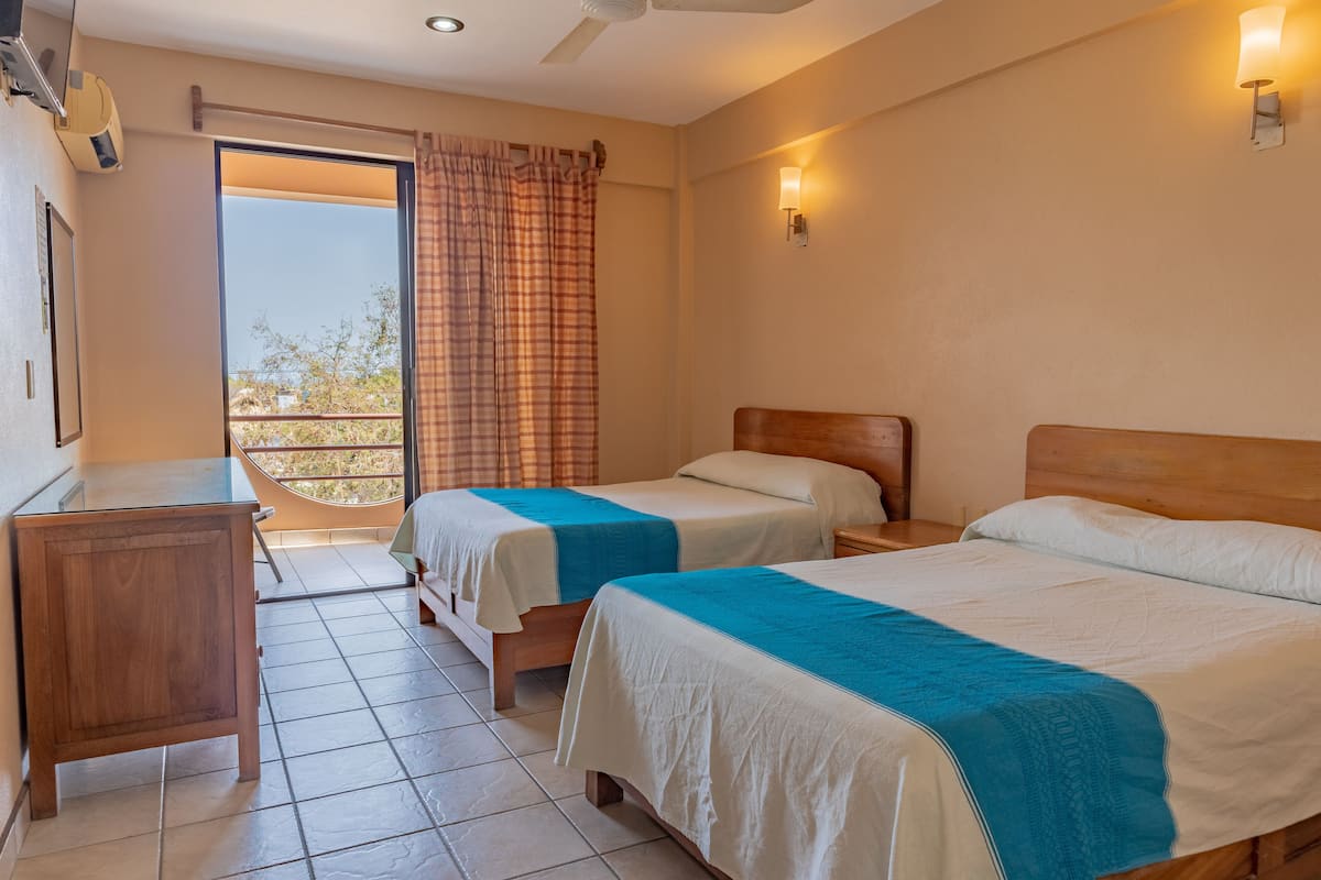 A hotel room with two beds, a wooden desk, a balcony with a view, and a sliding door.
