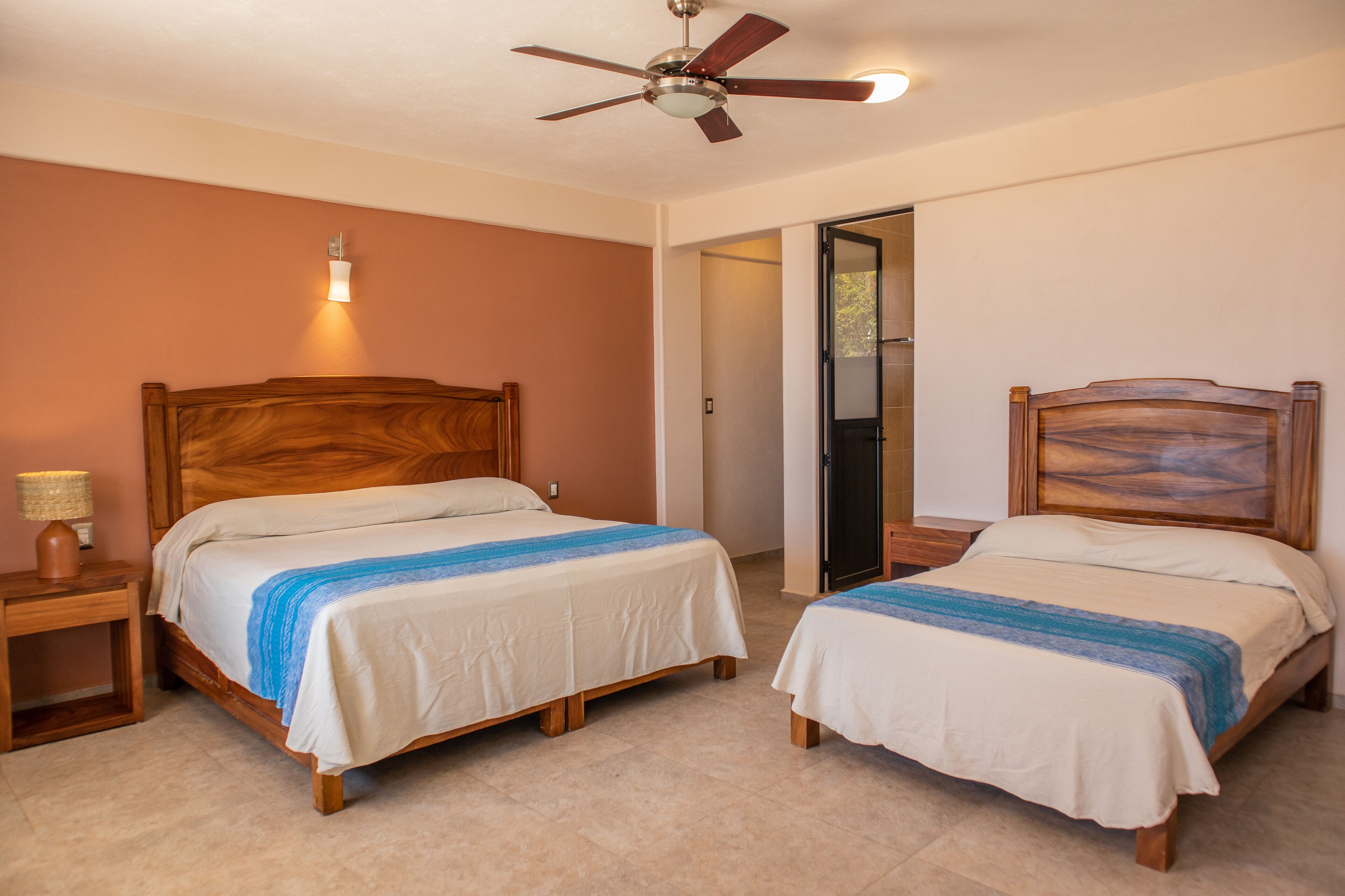 A bedroom with two wooden beds, a ceiling fan, and a nightstand with a lamp.