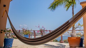 Una hamaca en un balcón con plantas en macetas y vista al mar.