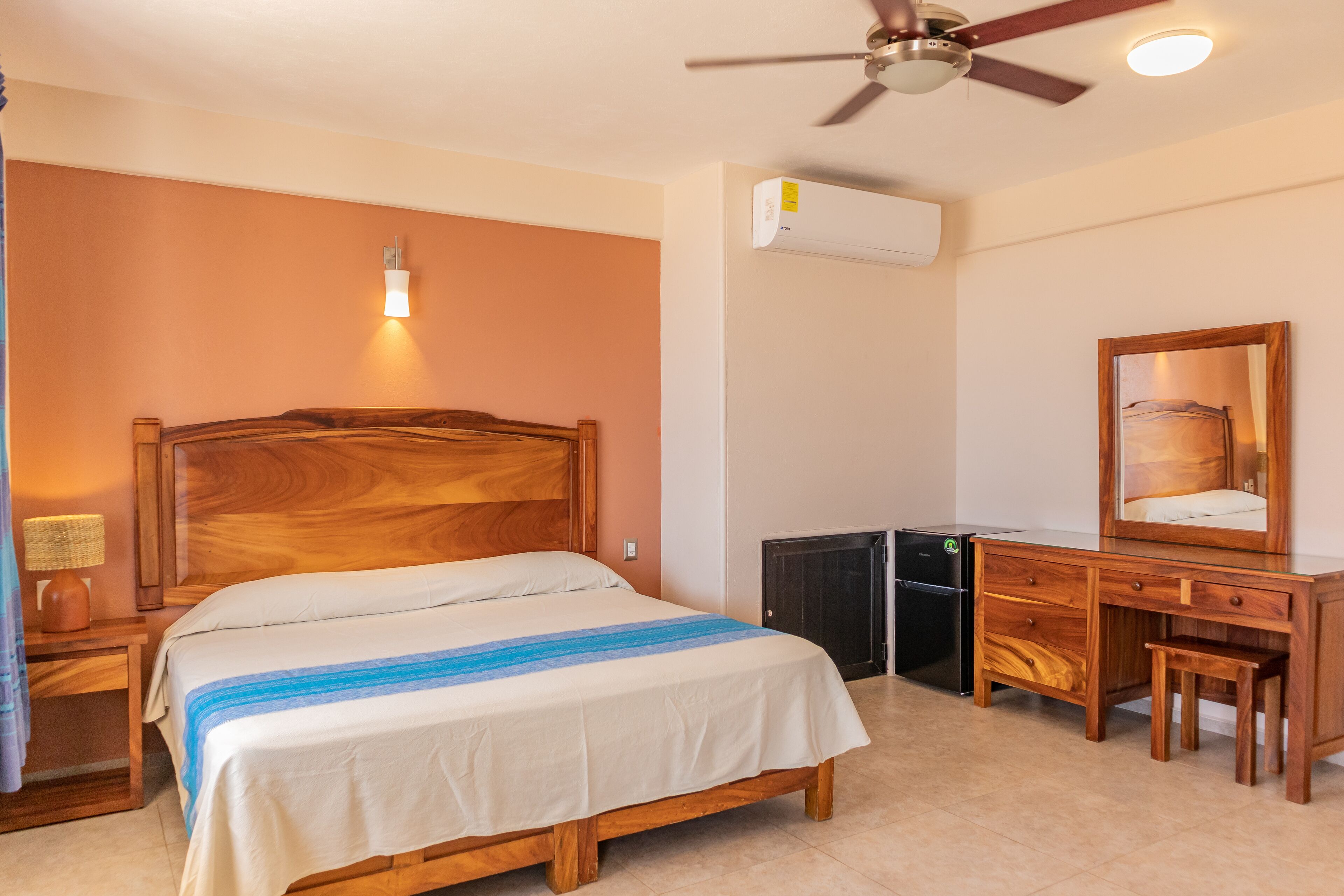 A bedroom with a wooden bed, a desk with a chair, a ceiling fan, and an air conditioning unit.
