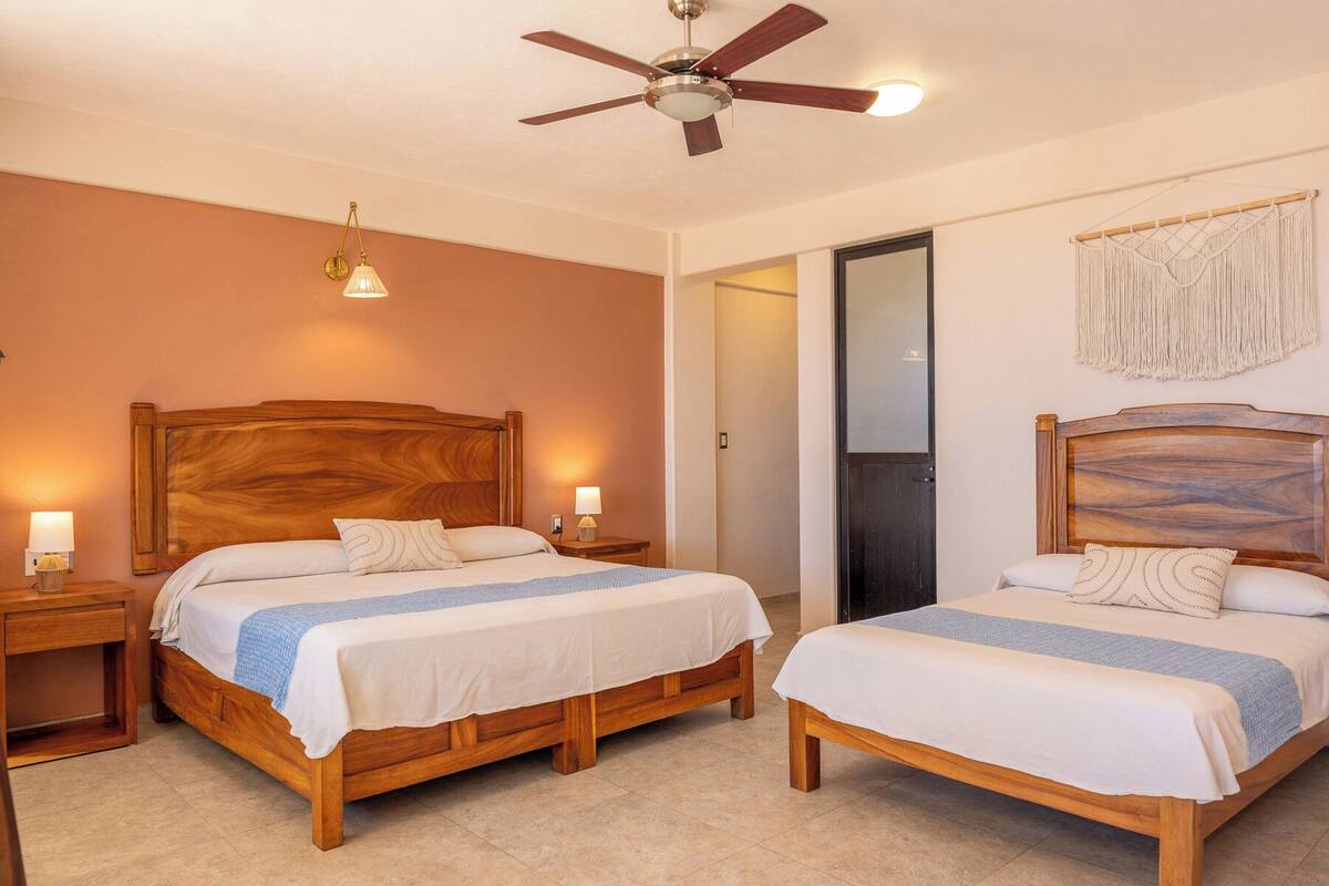 A hotel room with two wooden beds, a ceiling fan, and a macrame wall hanging.