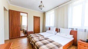 Habitación de hotel con dos camas, suelo de madera, un armario, una mesita de noche y una ventana con cortinas.