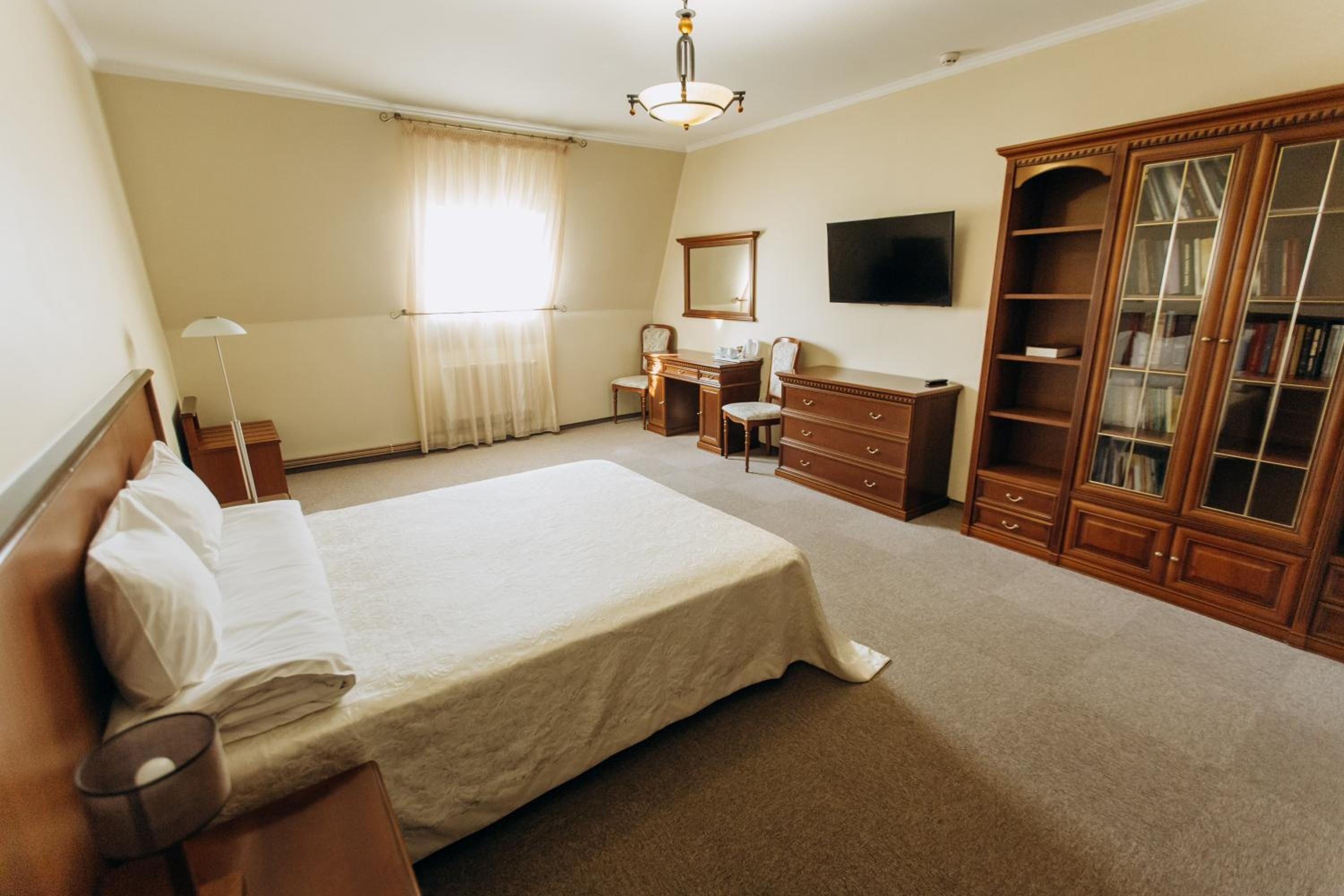 A bedroom with a large bed, a desk, a wardrobe, and a television on the wall.