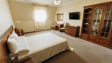 A bedroom with a large bed, a desk, a wardrobe, and a television on the wall.
