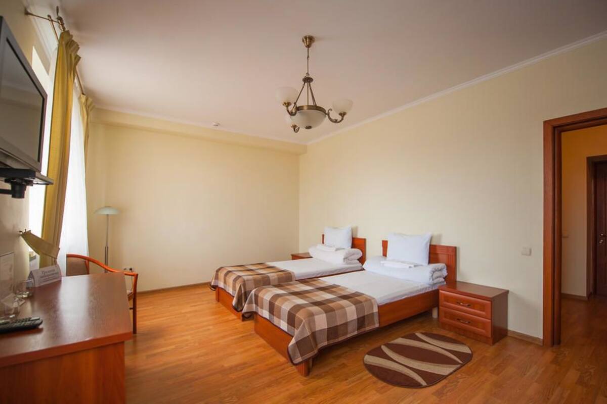 A hotel room with two beds, a desk, a chair, a TV, and a chandelier.