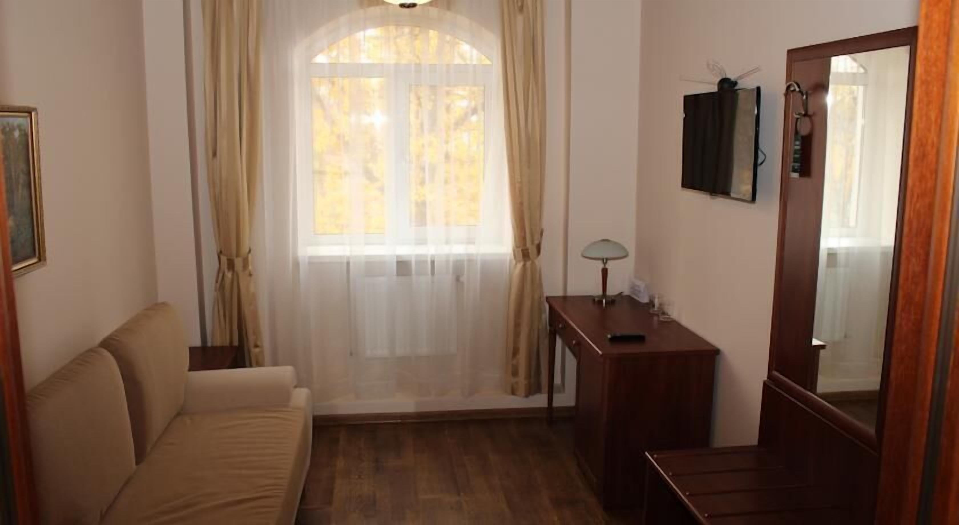 Quarto com sofá, mesinha de cabeceira com luminária, espelho e janela com cortinas.