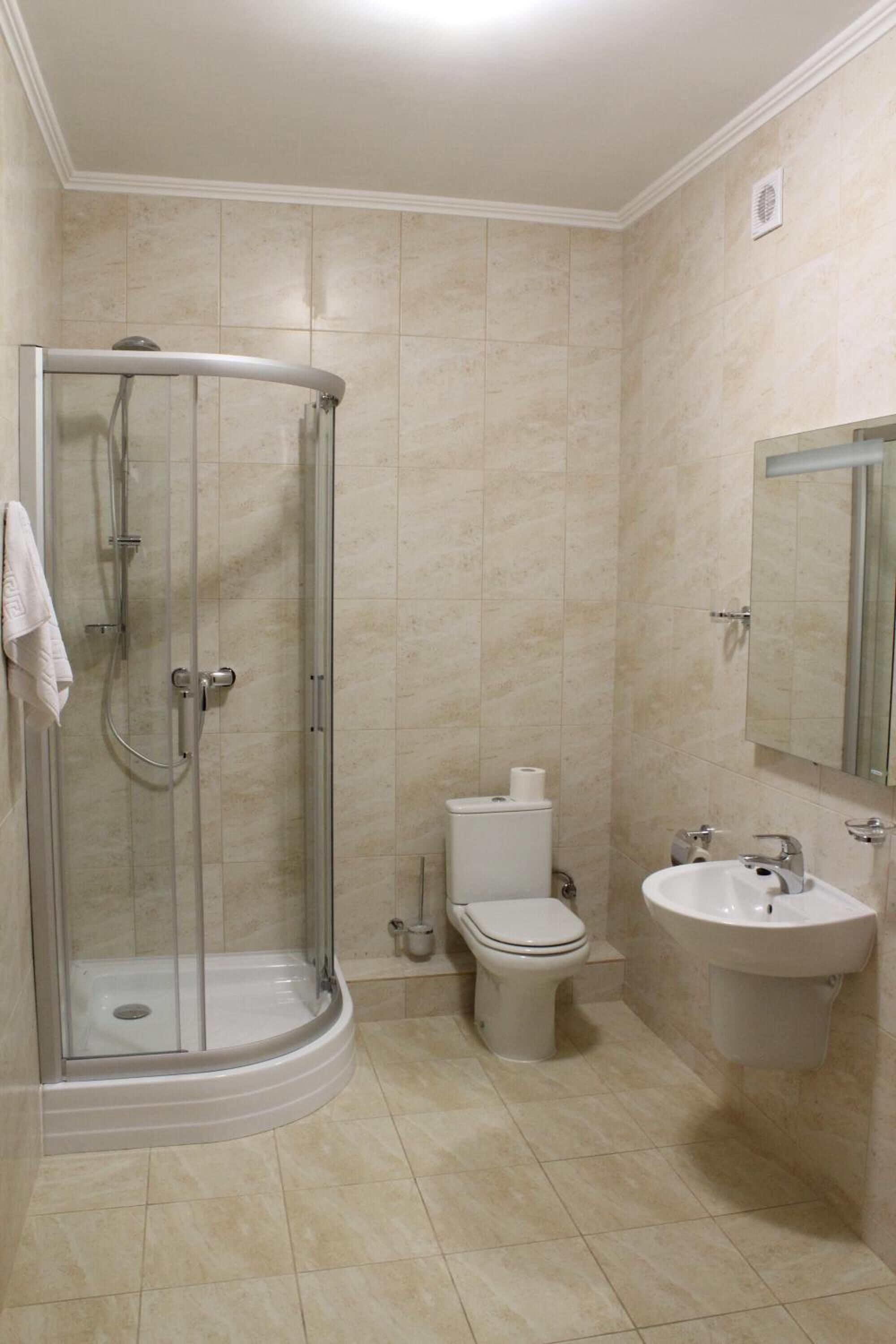 A bathroom with a glass shower enclosure, a toilet, and a sink with a mirror.